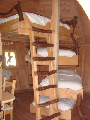 Les lits sont en suspension les uns au dessus des autres, en quinconce comme dans le principe d’un escalier en colimaçon. Le lit double est tout en haut, il est accessible par une échelle rigide. Les autres lits simples sont accessibles soit directement ou par une échelle souple. Cette configuration pour le moins originale permet d’avoir beaucoup d’espace dans cette cabane, d’où le coin détente crée avec des fauteuils.